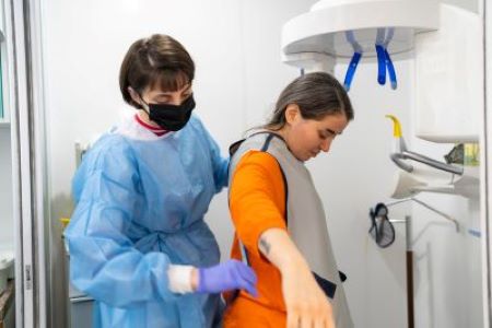 Woman wearing mask puts lead apron on patient before x-ray