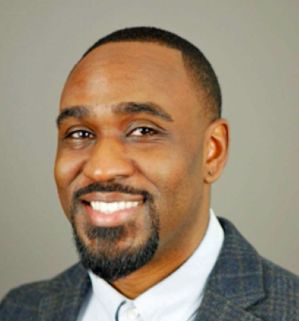 Patrick Smith Headshot – CareQuest Institute Professional Headshot of a Smiling Man in a Gray Blazer and White Shirt Against a Light Gray Background, Facing Forward.