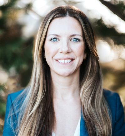Chelsea Chokas Headshot – CareQuest Institute Head-and-shoulders Portrait of a Smiling Woman with Long Brown Hair and a Blue Blazer, Outdoors.