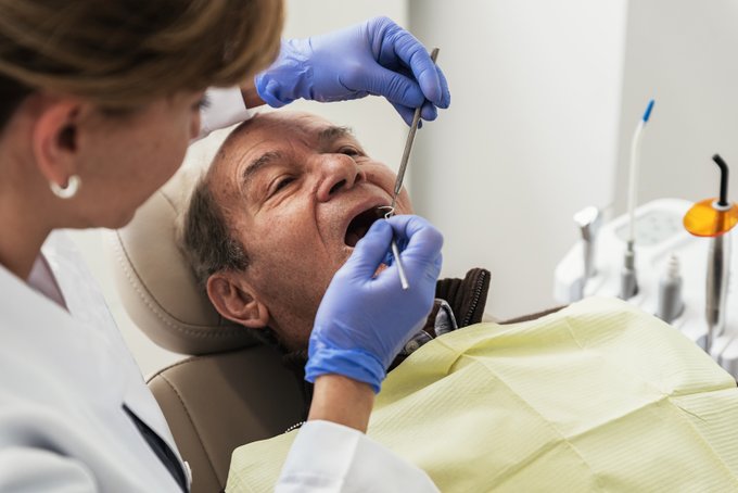 Dentist in Gloves Performing Dental Work on an Elderly Patient in a Chair in a Dental Office.