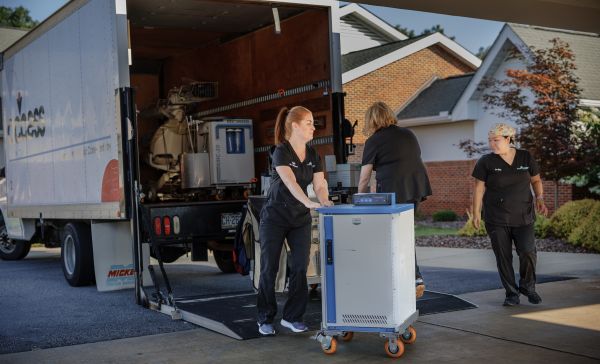 Access Dental equipment – CareQuest Institute Technicians Unload Equipment from a Service Van Using a Blue Cart in a Driveway.