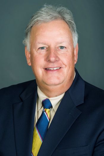 Daniel McNeil – CareQuest Institute Portrait of a Smiling Older Man with Gray Hair in a Navy Suit and Striped Tie.