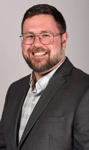 Harold Jennings Headshot – CareQuest Institute Smiling Man in a Gray Suit and Plaid Shirt, Wearing Glasses, on a Light Gray Background (professional Headshot).