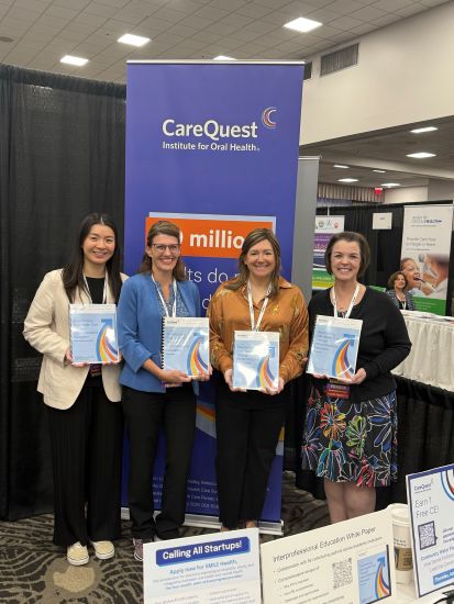 Four Women Stand Together at a Conference Booth, Each Holding a Report in Front of a Blue Carequest Banner, Smiling for the Camera.
