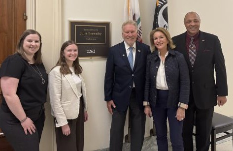 Five Adults in Business Attire Pose for a Photo in a Government Office, Standing Beside a Wall Plaque That Reads 'julia Brownley' with Two Flags in the Background.