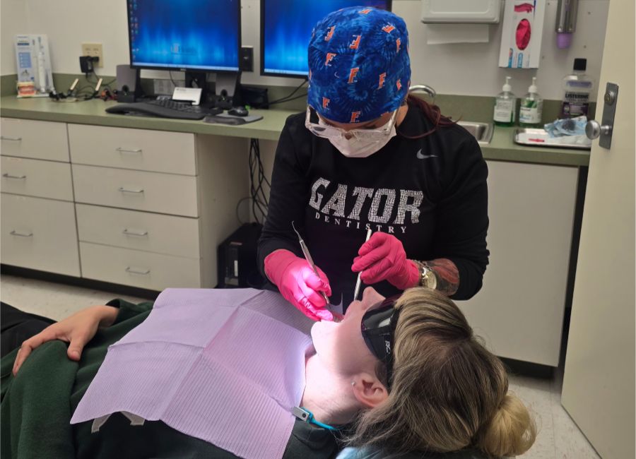 Mary Lynne Davis – CareQuest Institute Dentist Wearing a Blue Cap and Pink Gloves Treats a Patient in a Dental Chair.
