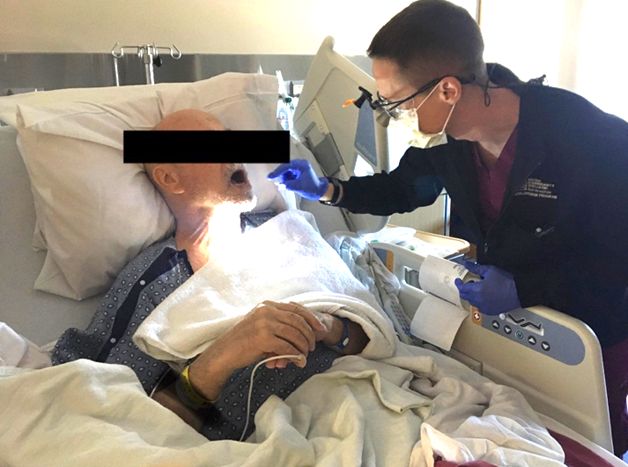 Nurse in a Medical Mask and Gloves Attending to an Elderly Patient in a Hospital Bed, Both Covered with Blankets.
