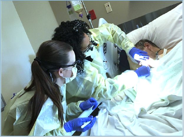 Two Healthcare Workers in Full Protective Gear Attending to a Patient in a Hospital Bed.