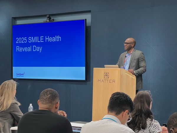 Wade at SMILE Reveal Day – CareQuest Institute Speaker in a Blazer at a Matter Podium Presenting to an Audience; Slide Reads '2025 Smile Health Reveal Day'.