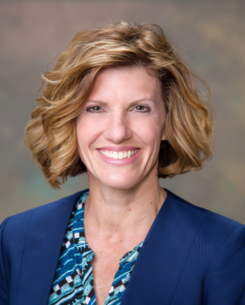 Professional Head-and-shoulders Portrait: Smiling Woman with Short Blonde Hair in a Blue Blazer Against a Soft Gradient Background.