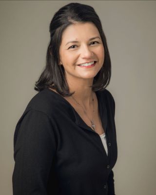 Portrait of a Smiling Woman with Shoulder-length Dark Hair in a Black Cardigan Against a Neutral Background.