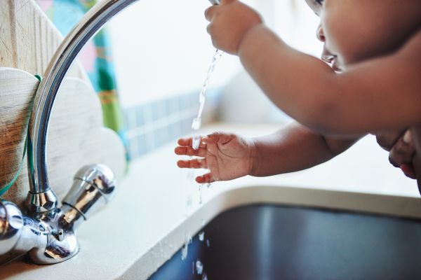Young Child Washes Hands Under a Running Faucet at a Sink in a Bright Kitchen Area.