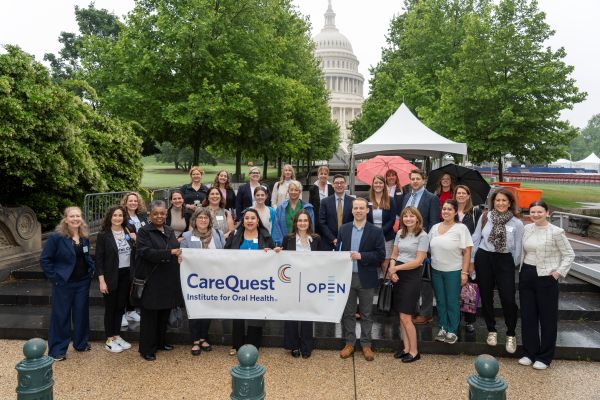 Diverse Group of Professionals Posing with a Carequest Open Banner Outside the U.s. Capitol Near an Event Tent.