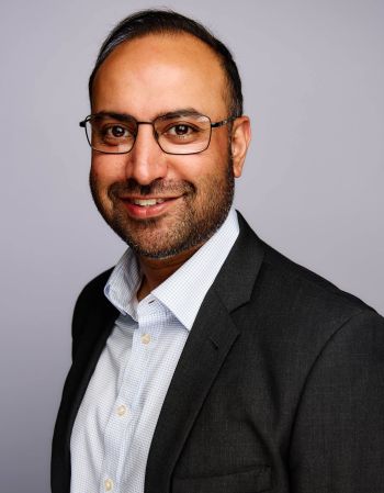 Professional Head-and-shoulders Portrait of a Man with Glasses, Wearing a Dark Blazer and Light Shirt, Smiling at the Camera.