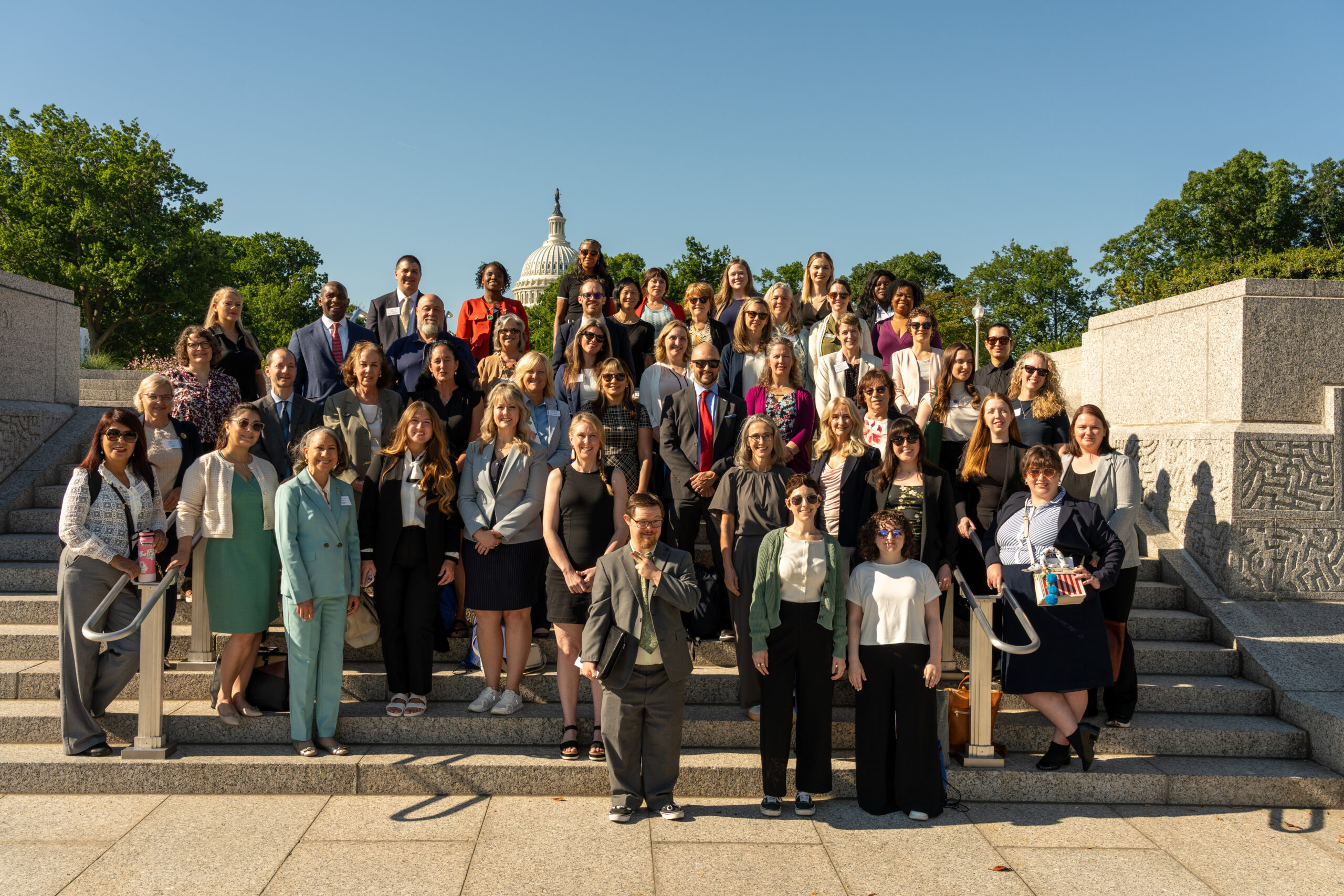Group of Diverse Adults Posing on Stone Steps with the U.s. Capitol Dome in the Background on a Sunny Day.