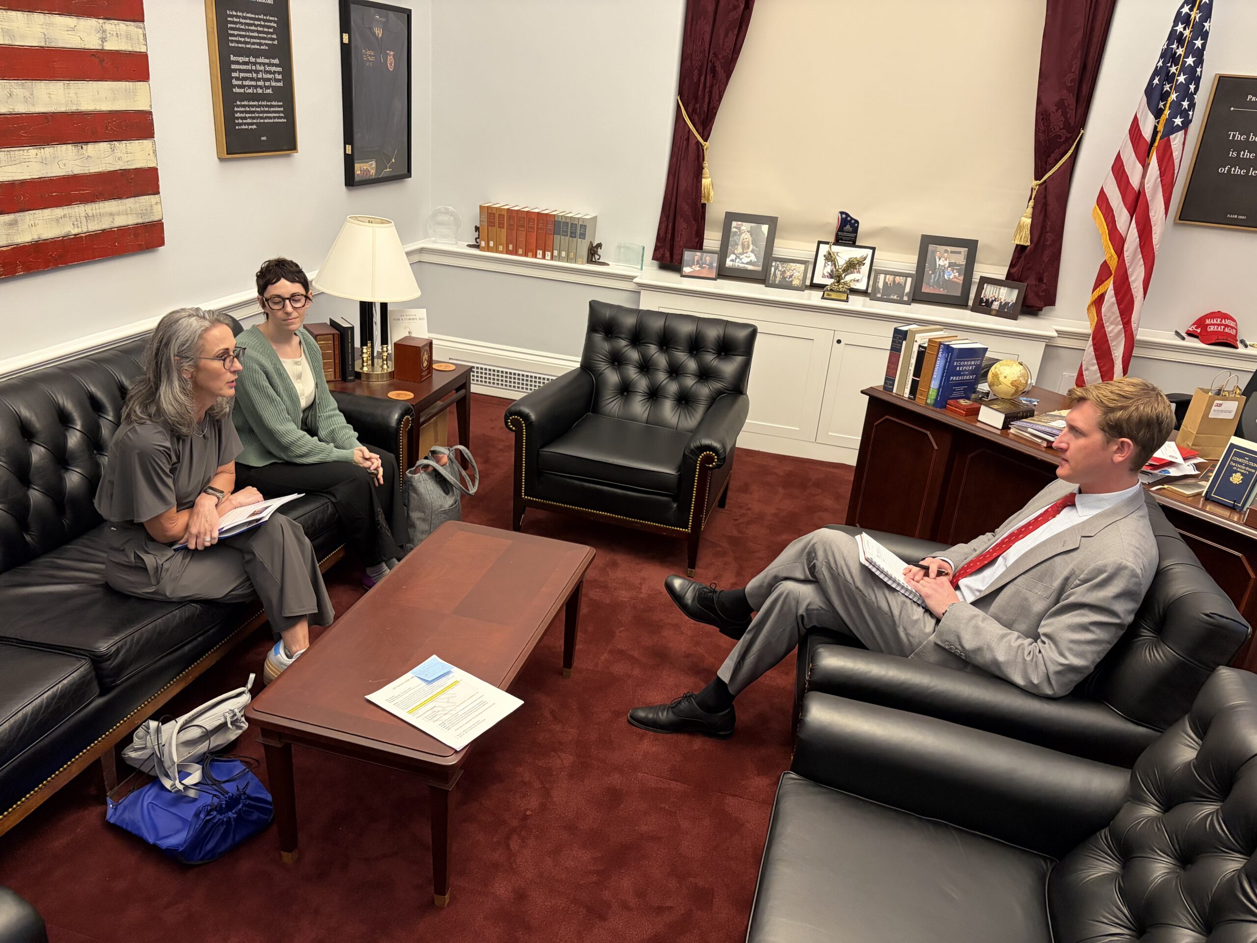 Office Scene with Three Adults Seated on Black Leather Sofas, a Wooden Coffee Table, and an American Flag in the Corner.] , but Not Allowed I Need to Fix.
