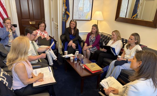 New Hampshire Advocates meet with Rep Goodlander – CareQuest Institute Group of Professionals Seated in a Government-style Conference Room Around a Coffee Table, Reviewing Documents; One Person on the Left Takes a Photo.