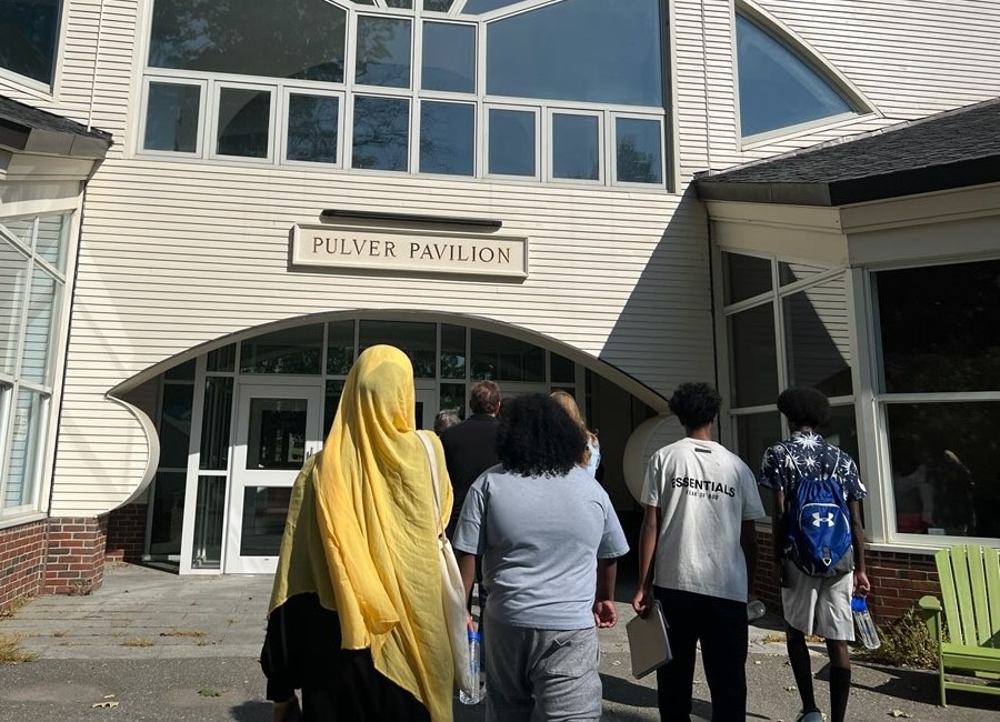 CHWs walking into building – CareQuest Institute Group of Students and Adults Walk Toward the Entrance of Pulver Pavilion, a Light-colored Building with a Curved Archway and Large Windows.