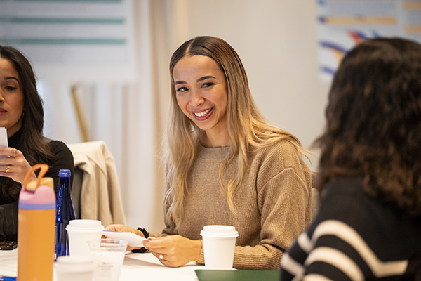 Young Woman with Long Blond Hair Smiling at a Table in a Meeting Room, with Cups and Notebooks Nearby.