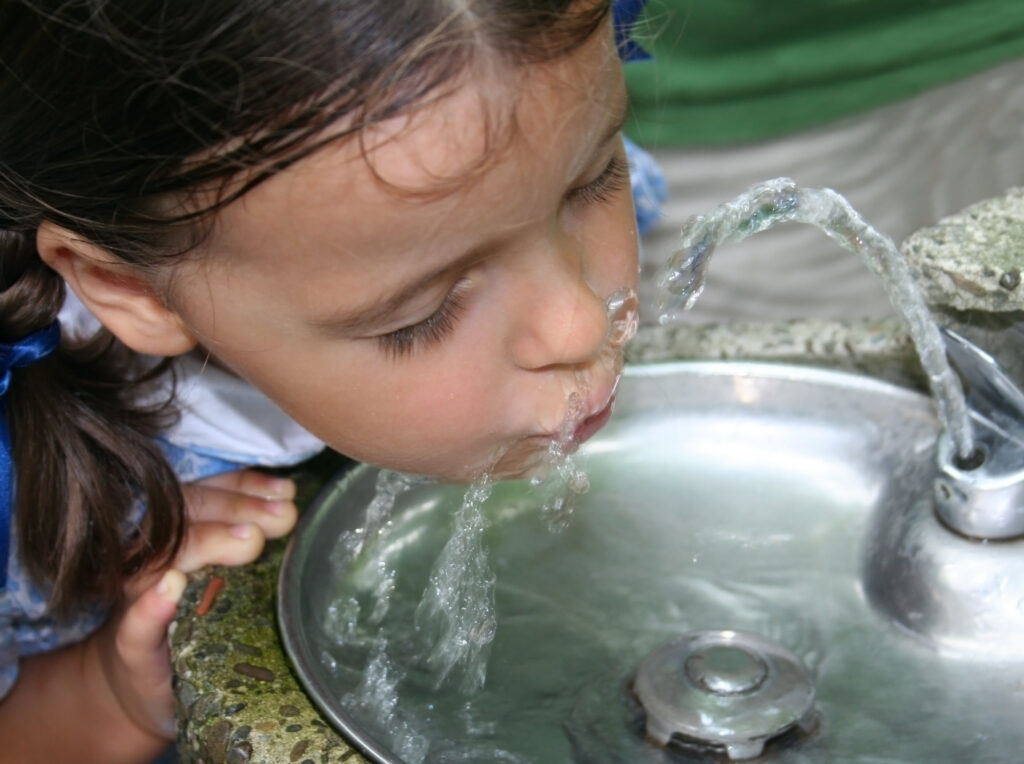 Close-up of a Young Girl with Her Eyes Closed, Drinking from a Outdoor Fountain Water Stream.