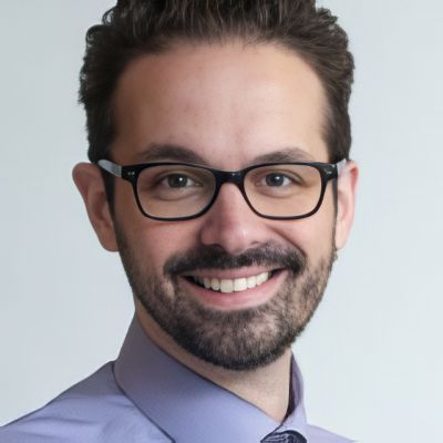 Smiling Man with Dark Hair and a Beard Wearing Black Rectangular Glasses and a Lavender Shirt, Portrait.
