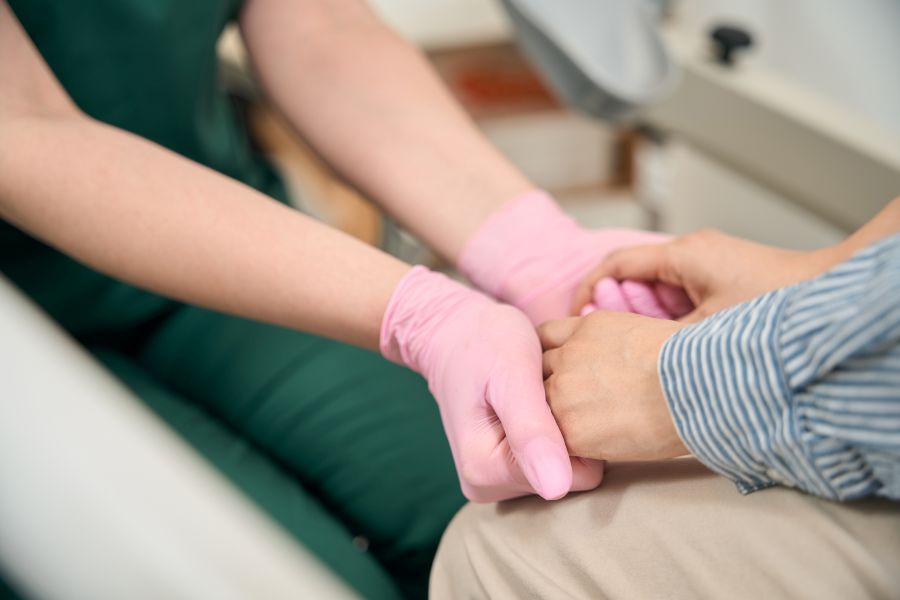 Caregiver Wearing Pink Gloves Gently Holds a Patient's Hand in a Clinical Setting to Provide Comfort and Support.